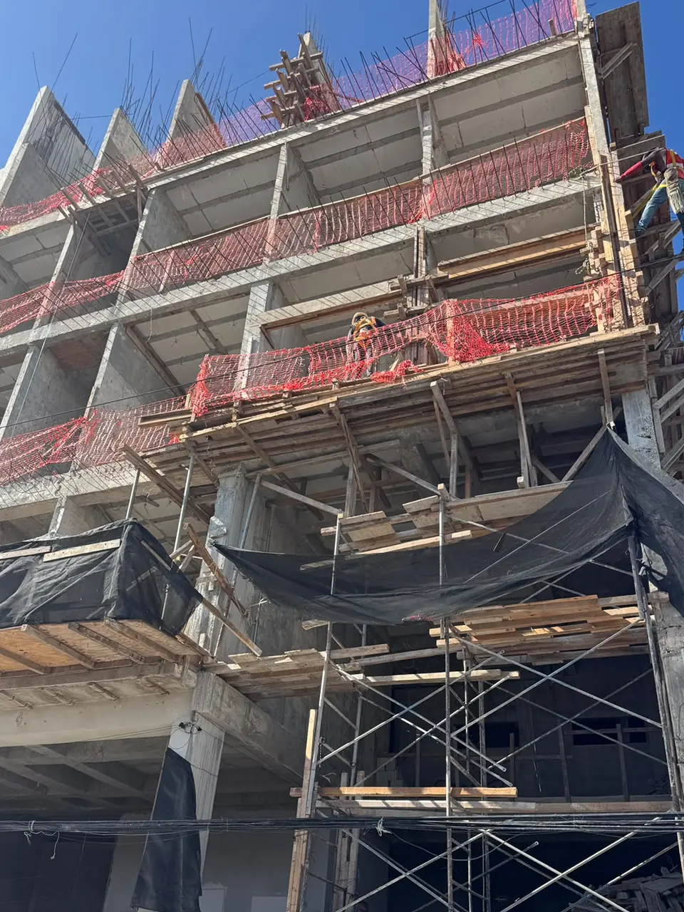 La torre de Amada Mía desde la calle en septiembre de 2026: la estructura levantada, los bordes de losa enmallados y la cuadrilla trabajando en los niveles altos