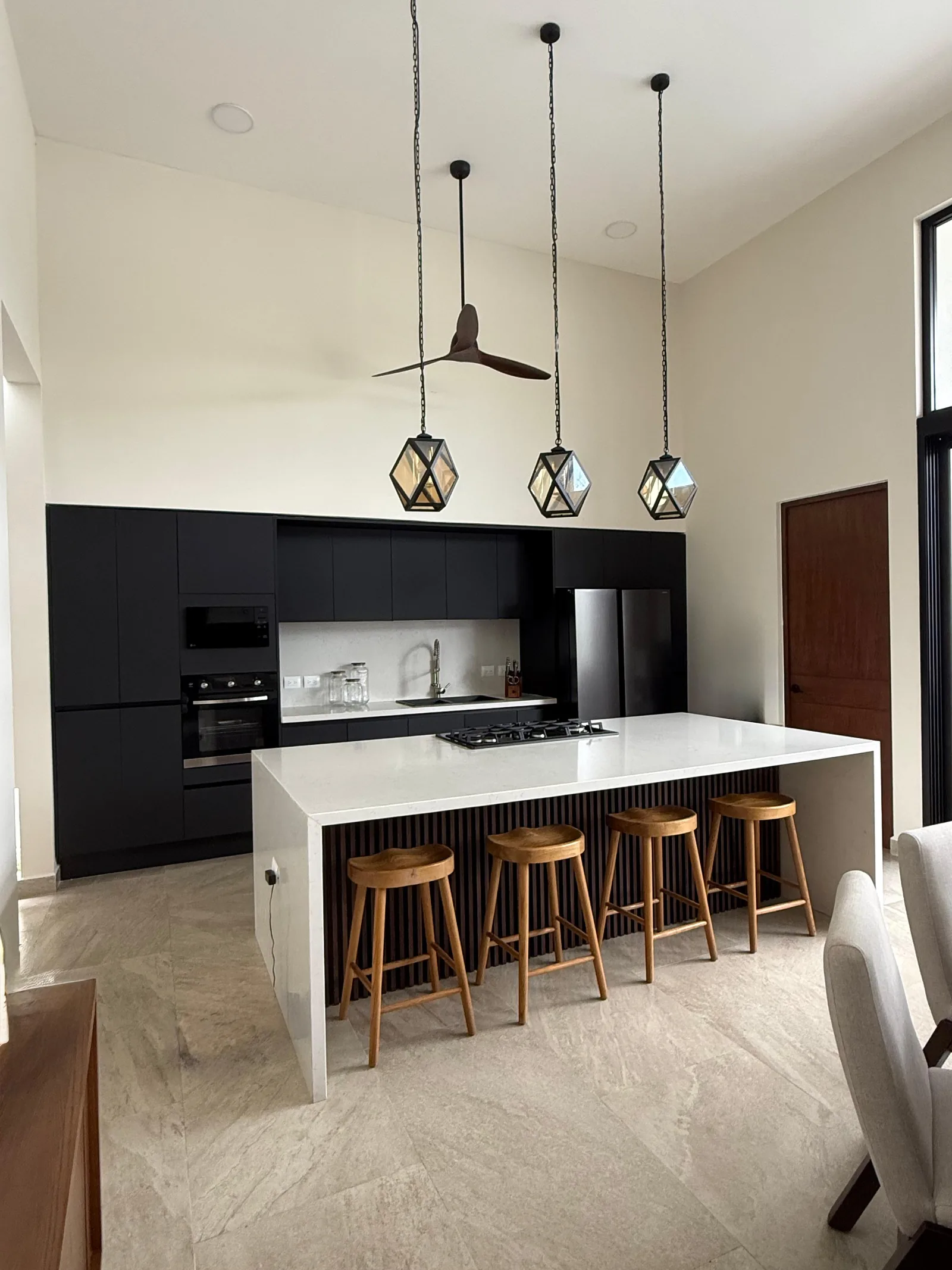 Cocina con isla de cuarzo, bancos y lámparas geométricas